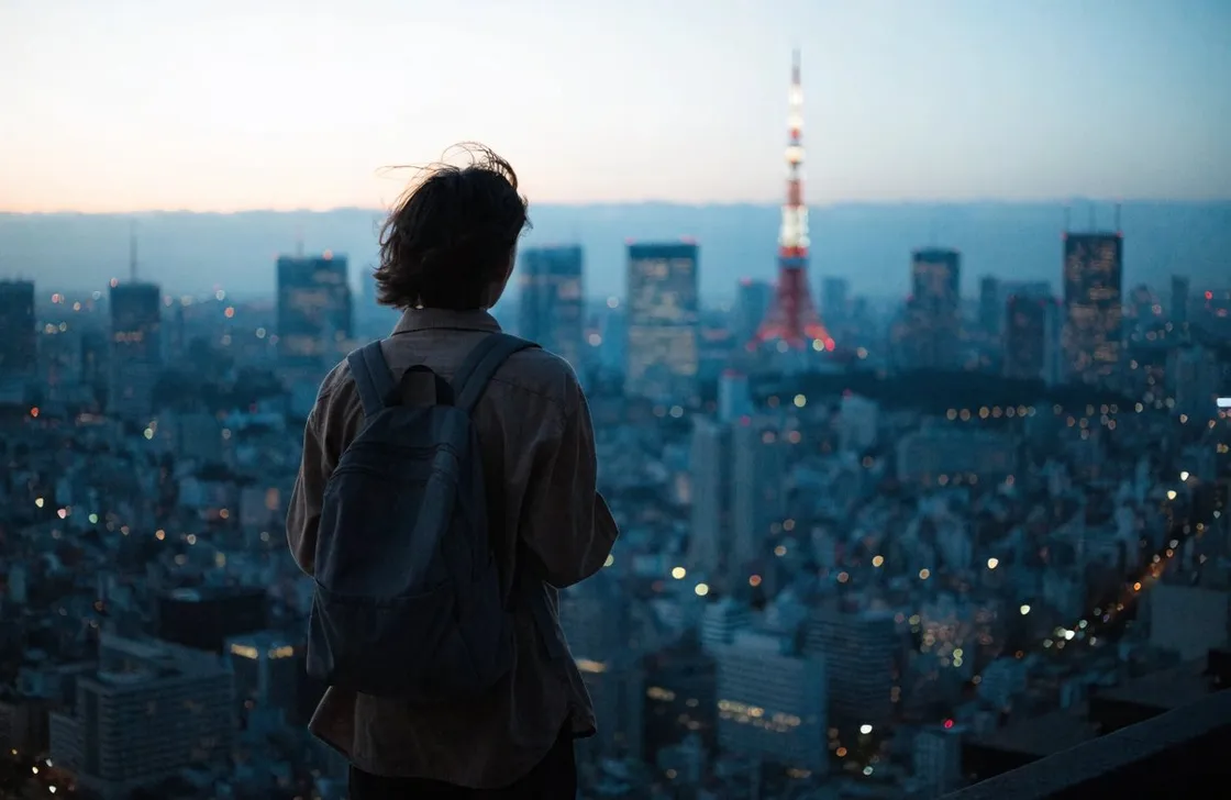 夕暮れの東京のスカイラインを見渡す、バックパックを背負った旅人